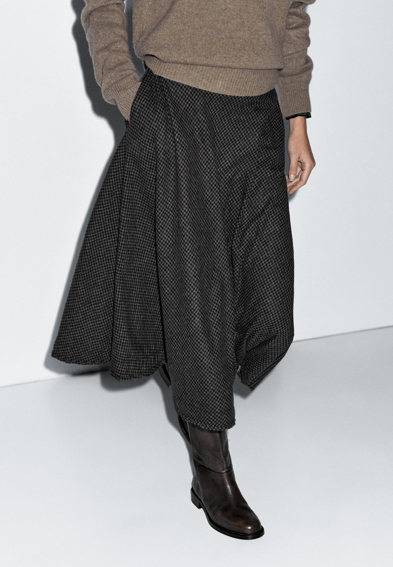 Schwarz-grau karierter Rock mit fließendem Design, kombiniert mit braunen kniehohen Lederstiefeln. Weiche Textur mit weiter Silhouette.