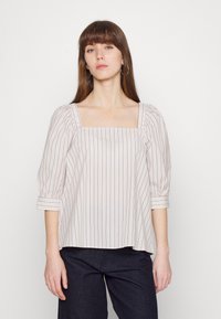 Blusa leve em creme com decote quadrado, riscas horizontais em azul-marinho, mangas bufantes e um corte relaxado. Textura suave com detalhes mínimos.