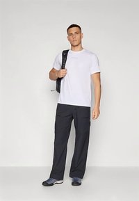 Bela majica s kratkimi rokavi z modrim napisom, črne hlače s cargo žepi in sive superge. Model nosi črn nahrbtnik na enem rami.