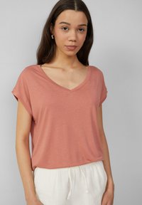 Rožu krāsas V-veida kakla T-krekls ar sarullētām īsām piedurknēm, izgatavots no mīksta auduma, kombinēts ar baltām biksēm ar aukliņu. Gluda tekstūra.