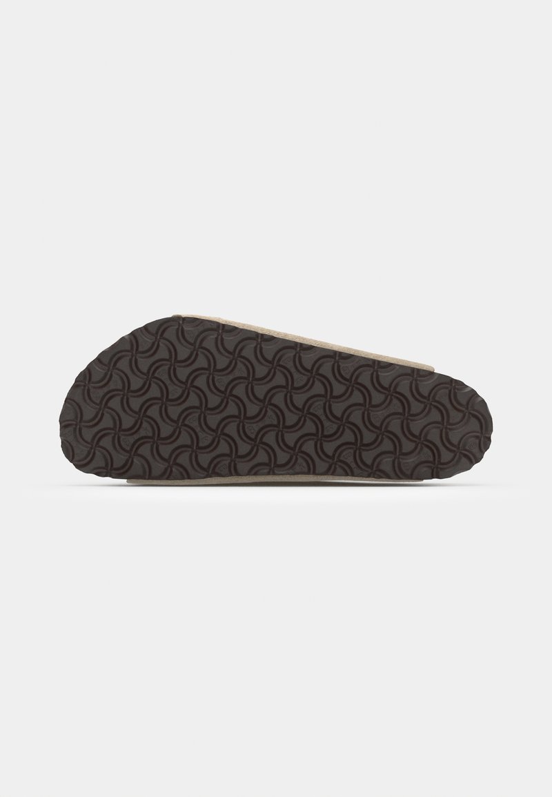Shoe outsole in dark brown rubber with a wave pattern; tan side accent. Light-colored upper edge with a smooth texture.