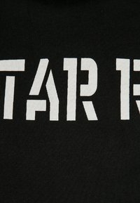 Tejido negro con grandes letras blancas en bloque que dicen "STAR R." La textura es suave y ligeramente elástica, con un diseño de punto cerrado.