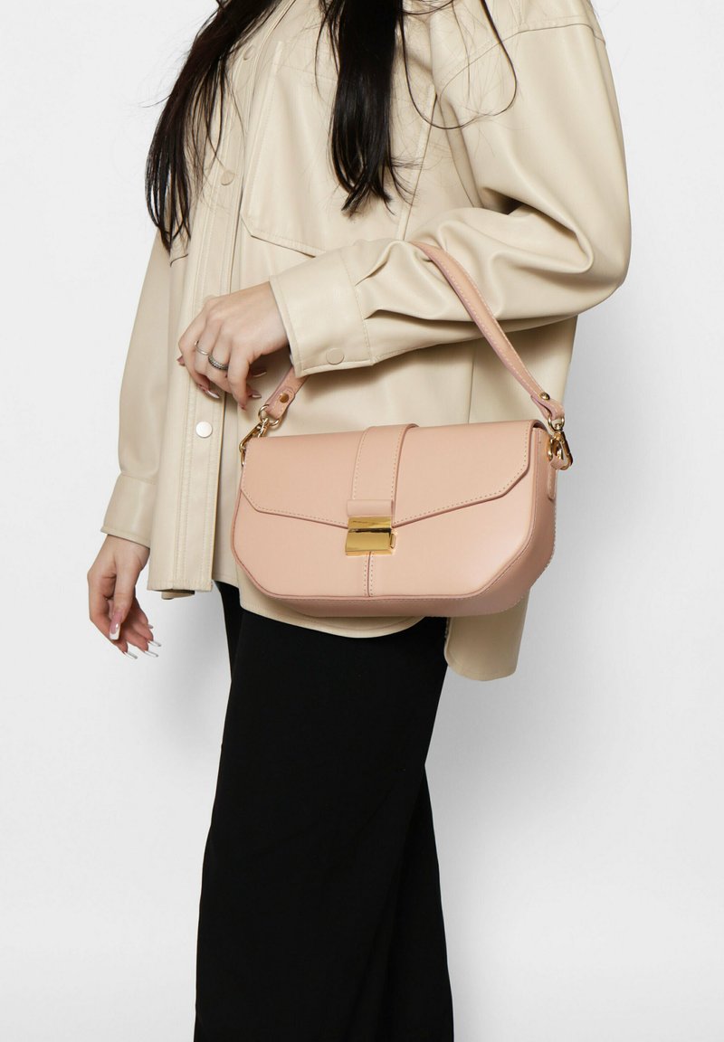 Borsa a tracolla in pelle rosa con design strutturato, dettaglio della chiusura dorata e tracolla, portata da una persona con una camicia in finta pelle color crema.