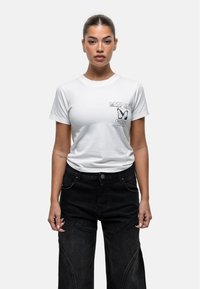 Witte katoenen t-shirt met een vlinderafbeelding en tekst op de linkerborst. Gekleed met zwarte wijde denim broek.