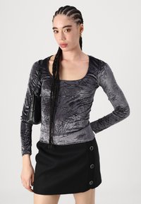 Grå crushed velvet langermet topp med rund hals, sammen med et kort svart skjørt med metallknappdetaljer.