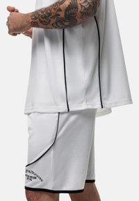 Witte sporttrui en shorts, met een gestructureerde stof, zwarte accenten en geborduurde tekstdetails op de shorts.