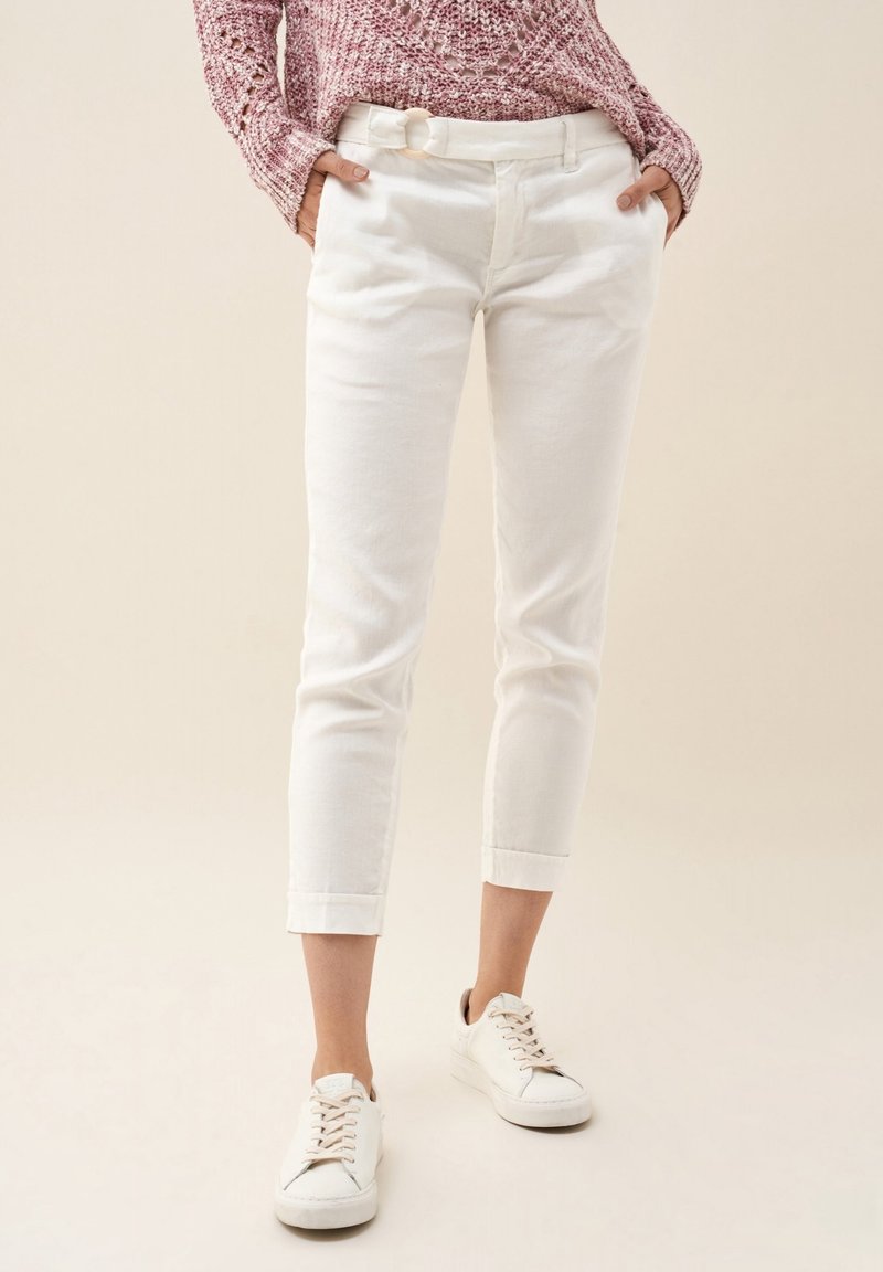 Pantalons blancs en coton, longueur cheville, avec une coupe slim, dotés de passants de ceinture et de revers, associés à des baskets blanches.