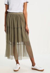 Falda maxi de gasa en capas y verde oliva con cintura elástica. Combinada con una camiseta de rayas y zapatillas blancas con suelas color canela.