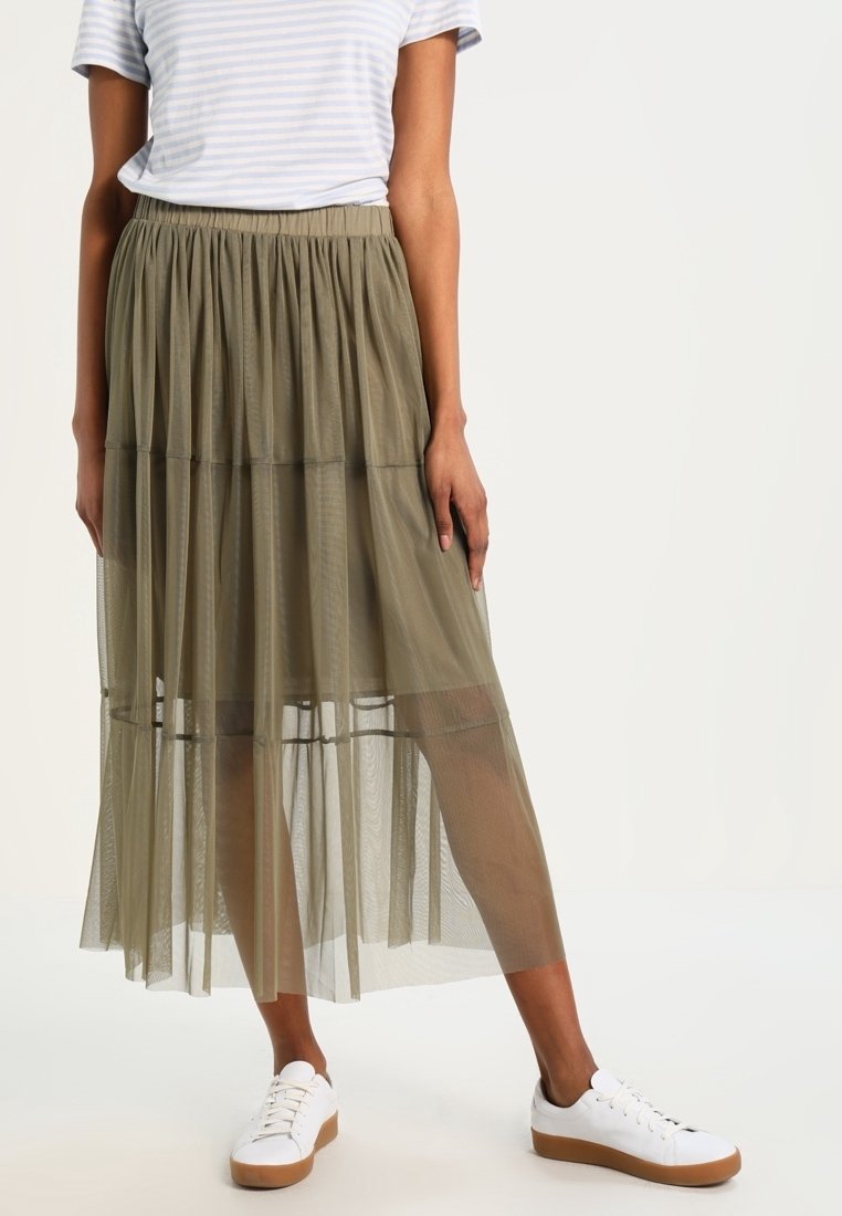 Falda maxi de gasa en capas y verde oliva con cintura elástica. Combinada con una camiseta de rayas y zapatillas blancas con suelas color canela.