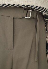 Pantalons khaki avec une coupe ajustée, dotés d'une large ceinture avec une boucle métallique, d'une texture de tissu lisse et de poches latérales.