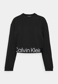 Svart kort sweatshirt med långa ärmar, som har en ribbad textur och en vit "Calvin Klein"-logotyp på nederkanten.