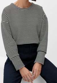 Top de manga larga a rayas blancas y negras con un escote amplio, con un corte cropped y tejido texturizado. Combinado con denim oscuro.