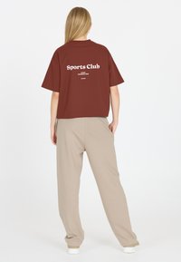 Bordeauxkortärmad t-shirt med texten "Sports Club", ihopparad med beige joggarbyxor. Mjuk tygkvalitet med avslappnad passform och utan synliga mönster.