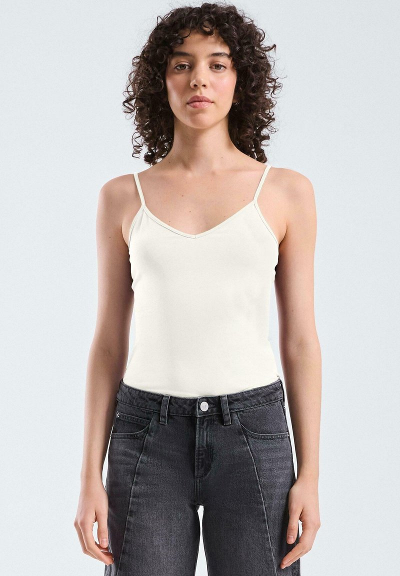 Witte hemdtop met dunne banden en een V-hals, gemaakt van zachte stof, gecombineerd met hooggepaste donkergrijze jeans. Eenvoudig ontwerp.