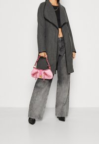 Harmaa pitkä takki, jossa avoin edusta, musta lyhyt toppi, löysät harmaat farkut ja pieni vaaleanpunainen käsilaukku, jossa on vetoketjuja ja teksturoitu pinta.