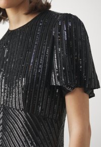 Robe noire avec des rayures verticales en sequins, des manches courtes bouffantes et une surface texturée. Effet scintillant notable et motif géométrique.