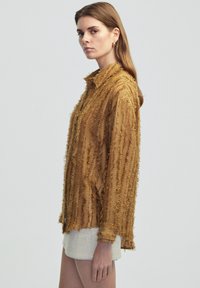 Fringed shirt in a warm brown hue, featuring a loose fit, textured fabric, and a collared design for added detail.