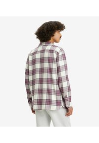 Koszula flanelowa w kratę w odcieniach bieli i fioletu, z mankietami na guziki, klasycznym kołnierzykiem i lekko zaokrąglonym dołem dla wygody.