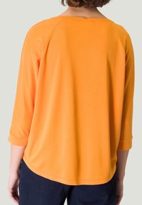 Oranges, Jersey-Oberteil mit drei Viertelärmeln und runder Ausschnittform sowie einem lockeren Schnitt. Der Stoff ist glatt mit leichtem Glanz und hat einen leicht geschwungenen Saum.