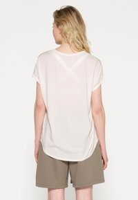 Lys beige kortærmet t-shirt med rund halsudskæring, blød tekstur og en buet kant. Båret med mørke khaki shorts.
