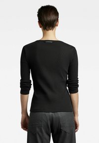 Schwarzes, geripptes Langarmoberteil mit einem runden Ausschnitt und hochgerollten Ärmeln. Mit einem Logosticker auf der Rückseite. Weiche Textur und taillierte Silhouette.