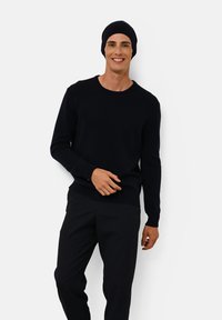 Donkerblauwe gebreide trui met een ronde halslijn en lange mouwen, gecombineerd met bijpassende donkere broek en een aansluitende beanie. Soepele textuur.