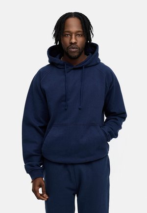 Navy blue hoodie made of soft fabric with a front kangaroo pocket, adjustable drawstring hood, and ribbed cuffs, worn with matching pants.