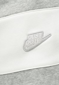 Γκρι και λευκό ύφασμα με κεντημένο το λογότυπο Nike και τη φράση "JUST DO IT." με κλωστή σε ταιριαστό γκρι χρώμα.