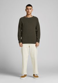 Olijfgroen gebreid sweater met een ronde hals, gecombineerd met off-white tapered broek en bruine schoenen met witte veters. Eenvoudig ontwerp en textuur.