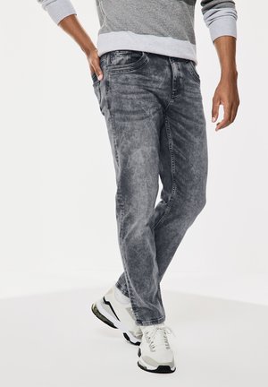Jeans de mezclilla gris con un acabado desvaído. Presentan un corte relajado, diseño de cinco bolsillos y detalles de costura sutiles. Combinados con zapatillas blancas.