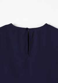 Granatowa bluzka z zapięciem na guziki z tyłu, z małym otworem w kształcie klucza oraz gładkiego, lekkiego materiału.