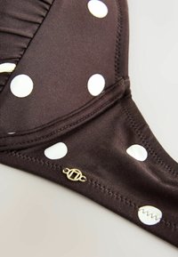 Top bikini marrone con pois bianchi, tessuto texture, dettagli arricciati e un piccolo accento in oro vicino alla cucitura.