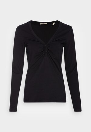 Top negro de manga larga con escote en V, detalles de botones y tela fruncida en el pecho, presentado sobre un fondo liso gris claro.