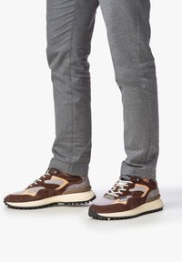 Braune und graue Sneaker aus Mesh und Wildleder, mit Schnürdesign, strukturiertem Profil und auffälligen Nähdetails.