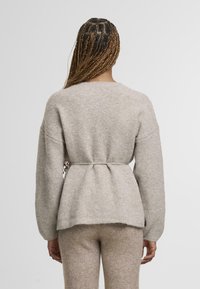 Jasnoszary, miękki sweter dziany z paskiem w talii, opuszczanymi ramionami i zaokrąglonym dekoltem. Tkanina wydaje się mieć teksturę i być przytulna.