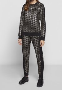 Svart loungedress med guld EA7-logotryck, bestående av en sweatshirt med rund hals och slim fit-byxor, båda med ribbad muddar och midja.