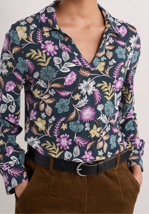 Blusa floreale con sfondo blu navy, fiori multicolori, colletto e maniche lunghe, abbinata a pantaloni in velluto a coste marroni e una cintura nera.