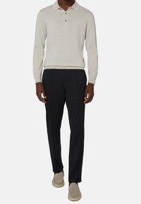 Svetle béžový pletený polo s dlouhým rukávem a límečkem, tmavě námořnické slim-fit kalhoty a béžové slip-on boty. Hladká textura, neutrální barvy.