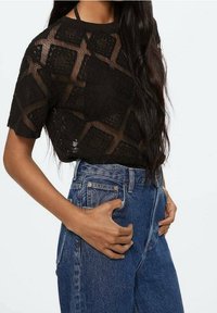 Black, short-sleeved knit top with a geometric pattern. Paired with high-waisted blue denim jeans. The fabric appears lightweight and breathable.