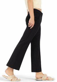 Pantalones de tiro ancho negros con bolsillos laterales. Fabricados en un tejido suave, presentan una cintura de media altura y detalles de costura sutiles. Combinados con zapatillas de felpa.