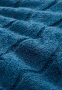 Tissu tricoté texturé de couleur bleu profond avec un motif ondulé, présentant une surface douce et duveteuse ainsi que des épaisseurs de fil variées pour un intérêt visuel.