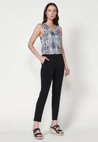 Tuta senza maniche nera con un top a motivi che presenta disegni geometrici in bianco e nero e tasche laterali; abbinata a sandali con zeppa neri.