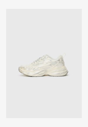 Biele bežecké tenisky s lesklým, štruktúrovaným povrchom. Obsahujú sieťové detaily, hrubú podrážku a reflexné prvky. Šnúrky sú v striebornom odtieni.