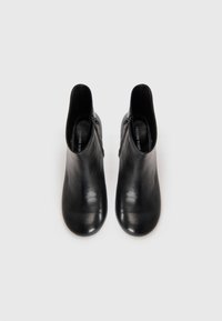 Black leather ankle boots with a smooth texture, rounded toe, and side zippers for ease of wear. Minimalist design and sleek shape.