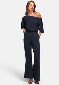 Marine off-shoulder top met vloeiende mouwen, gecombineerd met hoge taille, brede broek. De stof lijkt glad en lichtjes gestructureerd.
