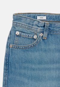 Løse denimjeans i lys blå. Funktioner: fem lommer, sølvhardware, kontrastsyning og et mærkat, der angiver "LOOSE."