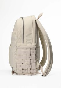 Mochila beige con un tejido suave, una textura tejida en el lateral, un bolsillo frontal con cremallera y correas ajustables acolchadas.