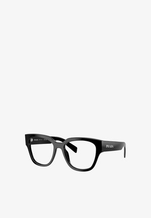 Lunettes en plastique noir à forme géométrique, avec une finition brillante et une marque Prada notable sur les branches.