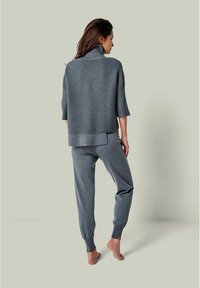 Grauer, gestrickter, oversized Pullover mit hohem Kragen, kombiniert mit passenden, schmal zulaufenden Sweatpants. Beide Teile haben eine weiche Textur und gerippte Details.