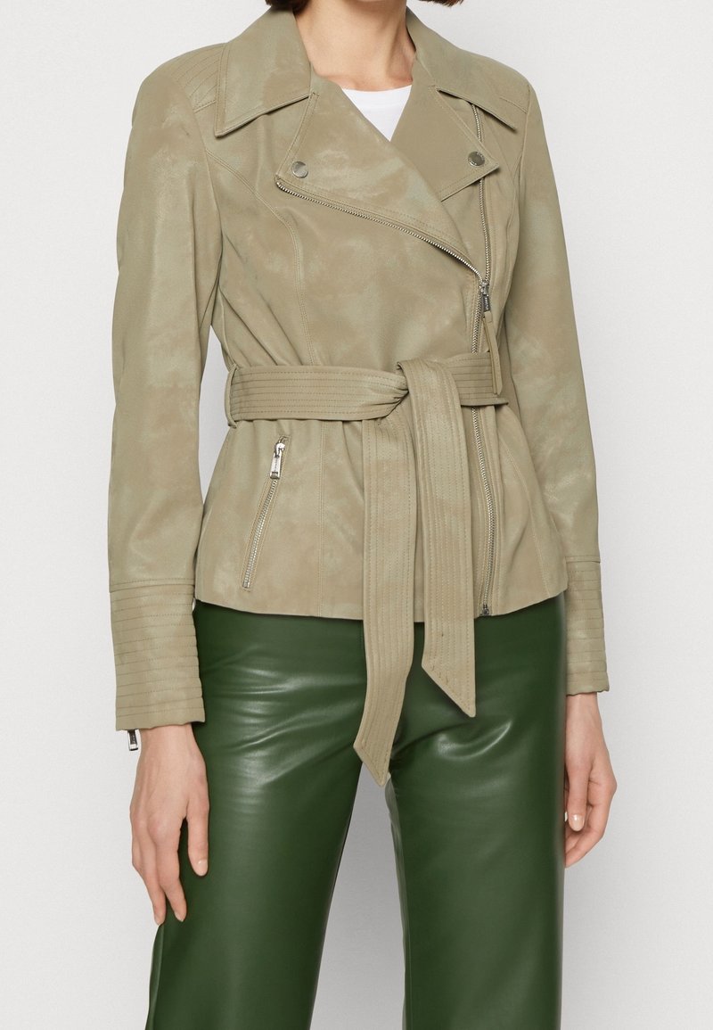 Veste de moto en simili cuir beige clair avec une taille ceinturée, des poches zippées et des détails en relief sur les manches.